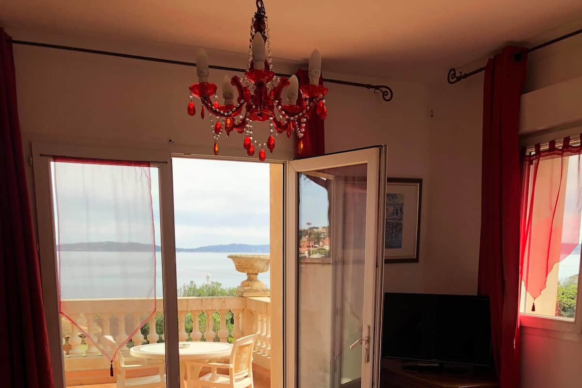 Une chambre avec un lit, une télévision, un balcon avec une table et des chaises, et une vue sur la mer.