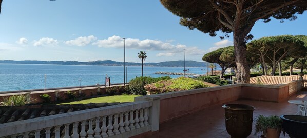 A terrace with a view of the sea, a stone balustrade, and potted plants.