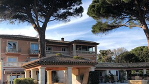 Un edificio de dos pisos con balcón, grandes árboles y un césped cuidado.