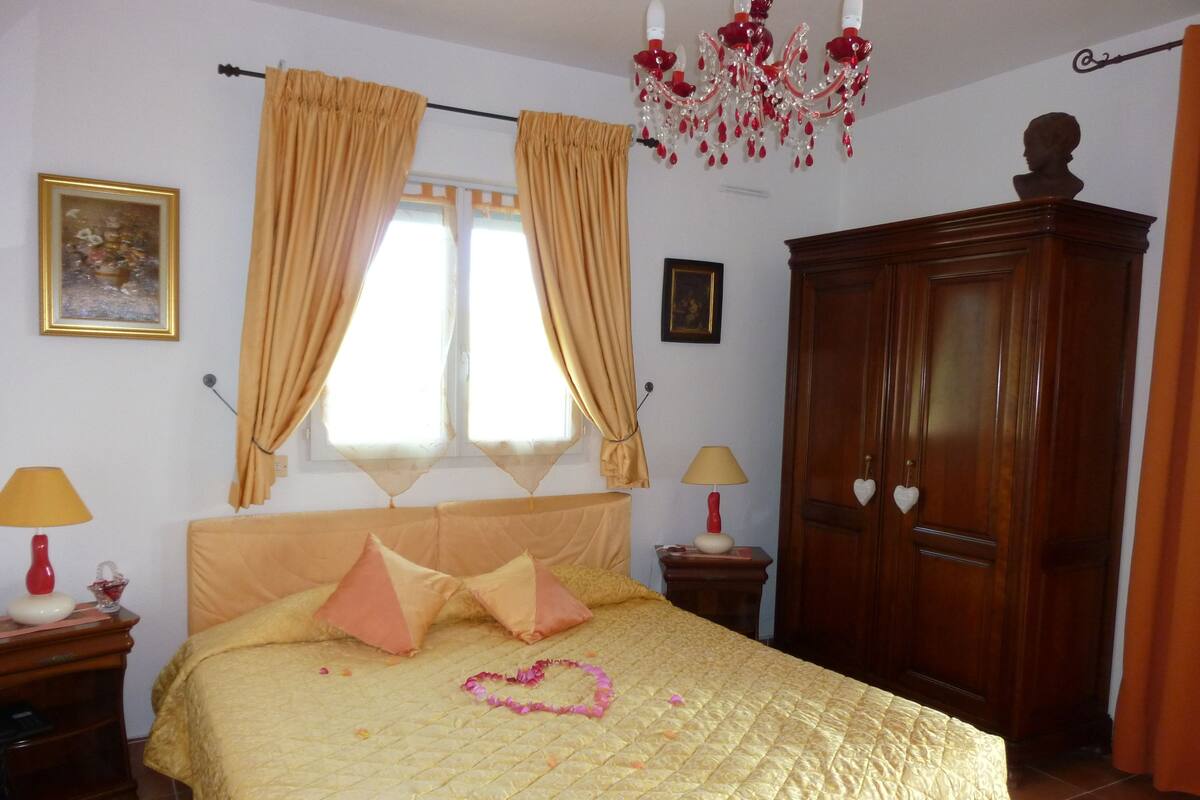Une chambre à coucher avec un lit, deux lampes de chevet, un lustre, une armoire et des rideaux.