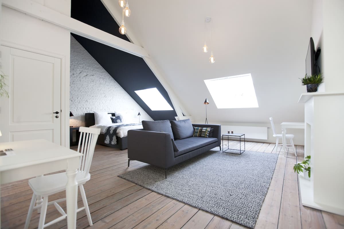 A loft-style room with a sloped ceiling, a gray sofa, a white dining table, and a small white chair.