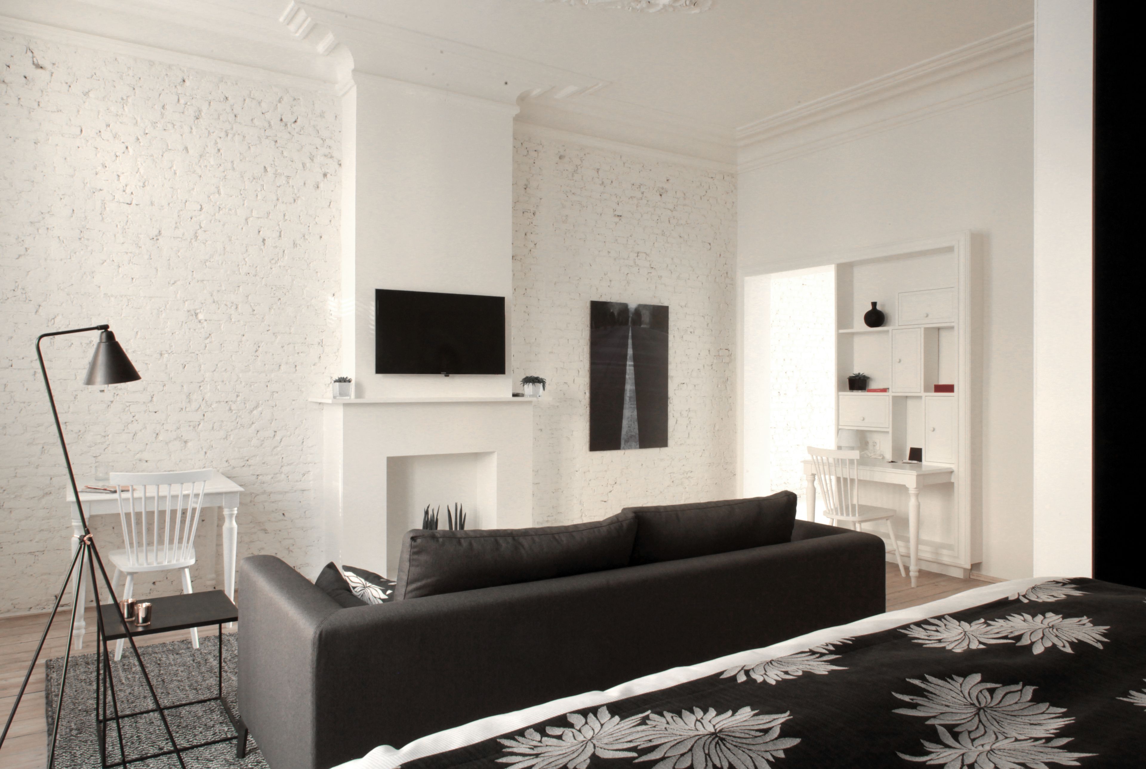 Een moderne slaapkamer met een zwarte bank, een wandtelevisie en een wit bureau.