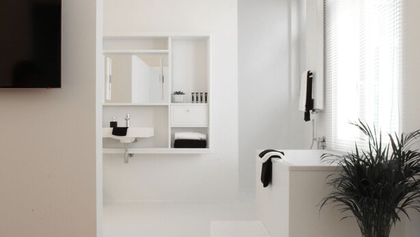 Een moderne badkamer met een wit wastafelmeubel, spiegel en een potplant.