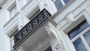 Een gebouw met een witte gevel, grote ramen en decoratieve ijzeren hekwerk.