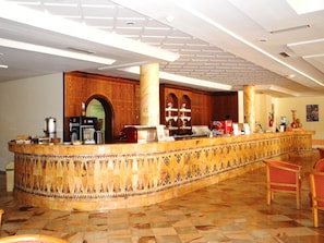 A hotel lobby with a curved reception desk, a coffee machine, and a Coca-Cola refrigerator. - Djerba Castille Hotel (Aghir)