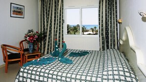 A bedroom with a bed, a chair, a table with a vase of flowers, and curtains. - Djerba Castille Hotel (Aghir)