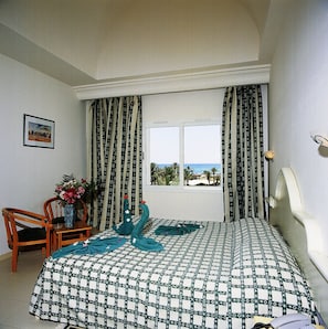 A bedroom with a bed, a chair, a table with a vase of flowers, and curtains. - Djerba Castille Hotel (Aghir)