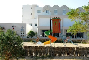 A playground with slides and climbing structures in front of a building with a white facade and a mural. - Djerba Castille Hotel (Aghir)