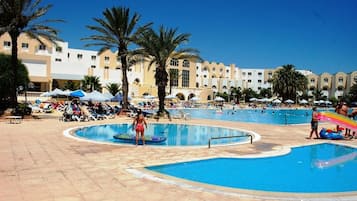 Zona d'una piscina d'hotel amb diverses piscines, gandules i palmeres.