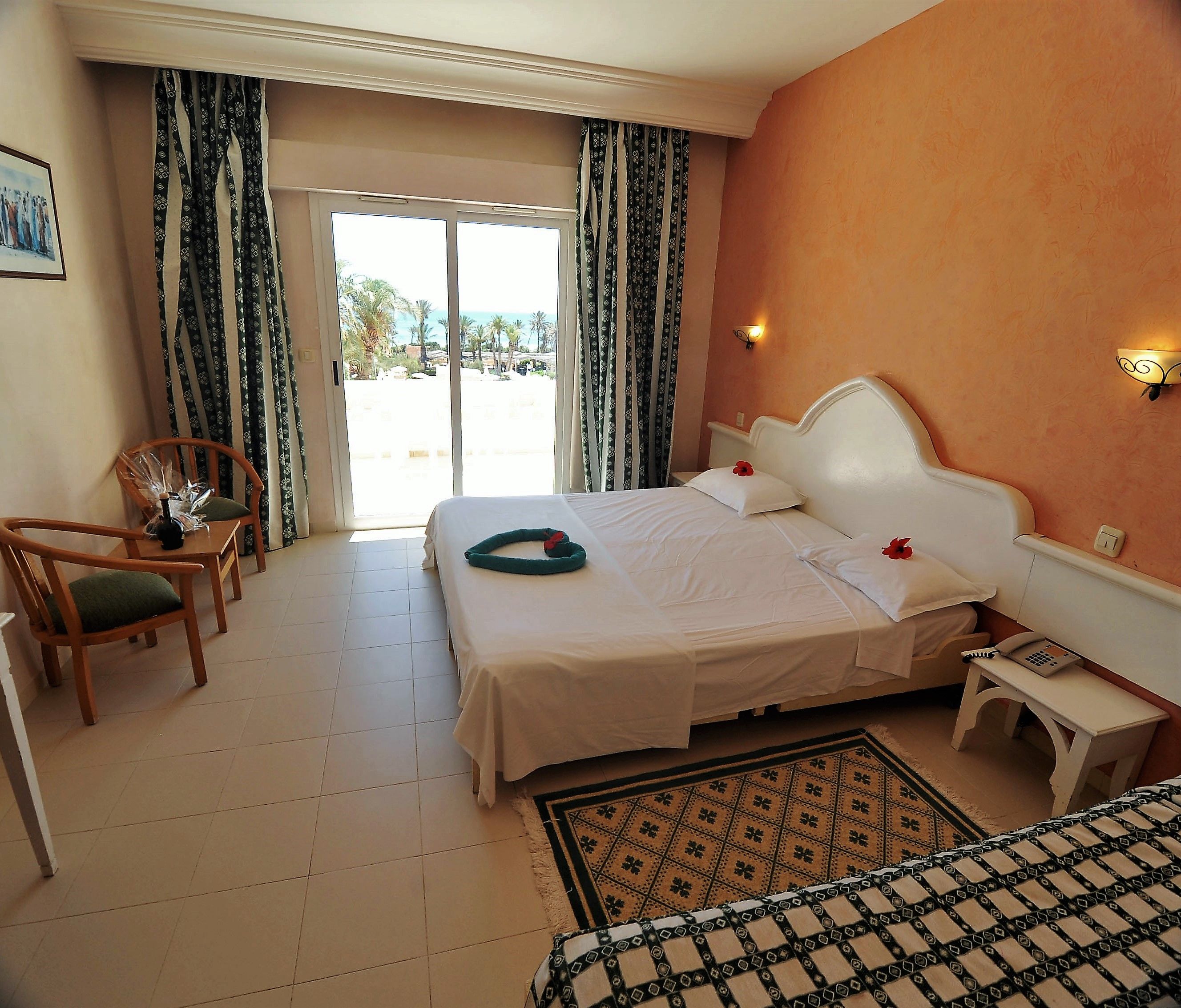 A hotel room with a bed, two chairs, a small table, a bedside table, a telephone, and a view of the outdoors.