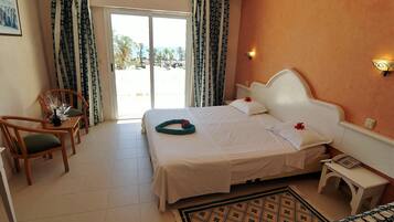A hotel room with a bed, two chairs, a small table, a bedside table, a telephone, and a view of the outdoors.
