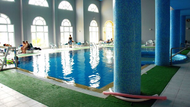 An indoor swimming pool with clear blue water, surrounded by large windows and blue-tiled pillars. - Djerba Castille Hotel (Aghir)