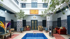A pool area with a blue tiled floor, two sofas, a table, and a decorative lamp. - Riad Azalia (Marrakech)