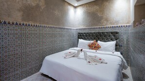 A hotel room with a bed, a tufted headboard, patterned walls, and a tiled floor. - Riad Azalia (Marrakech)