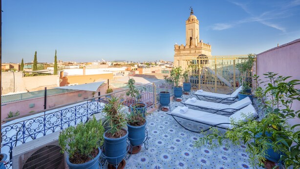 A rooftop terrace with lounge chairs, potted plants, and a view of a historic tower. - Riad Azalia (Marrakech)