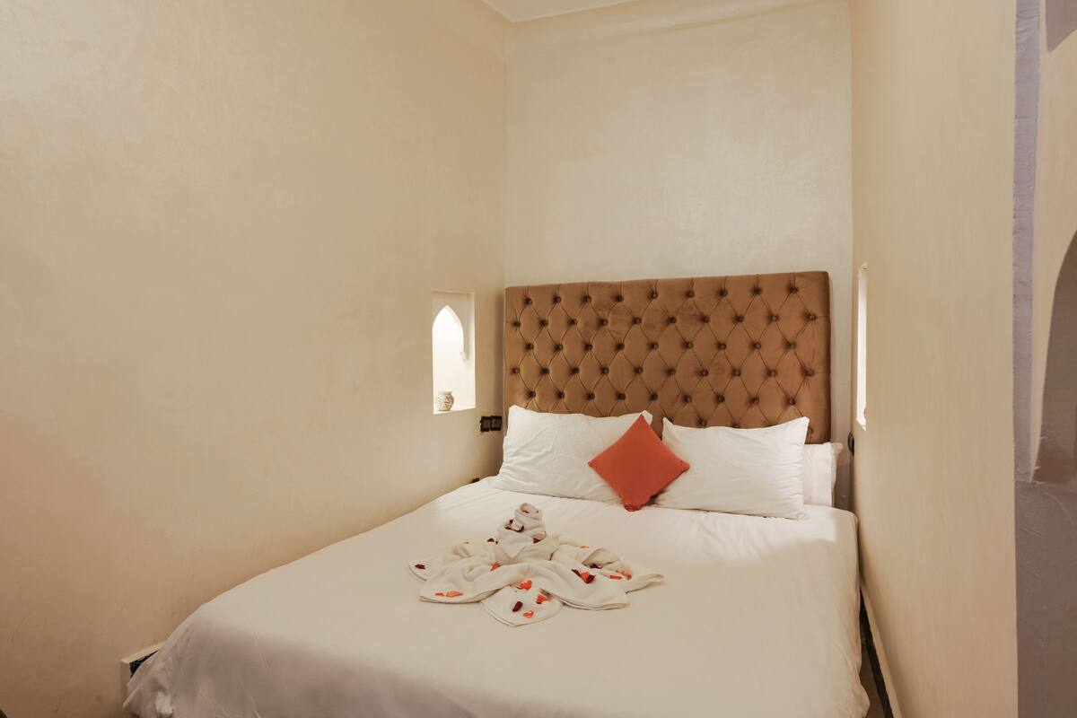 Cama bem arrumada com cabeceira estofada, roupa de cama branca e travesseiro vermelho.