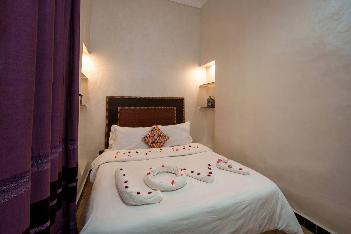 Uma cama bem arrumada com lençóis brancos, cabeceira de madeira e travesseiro decorativo.