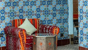 A room with a patterned blue and orange tiled wall, a sofa with a patterned cushion, and a small table. - Riad Azalia (Marrakech)