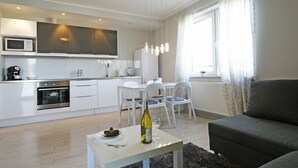 A modern kitchen with white cabinets, a built-in microwave, and a dining area with a table and chairs. - IRS ROYAL APARTMENTS - IRS Albatros (Gdansk)
