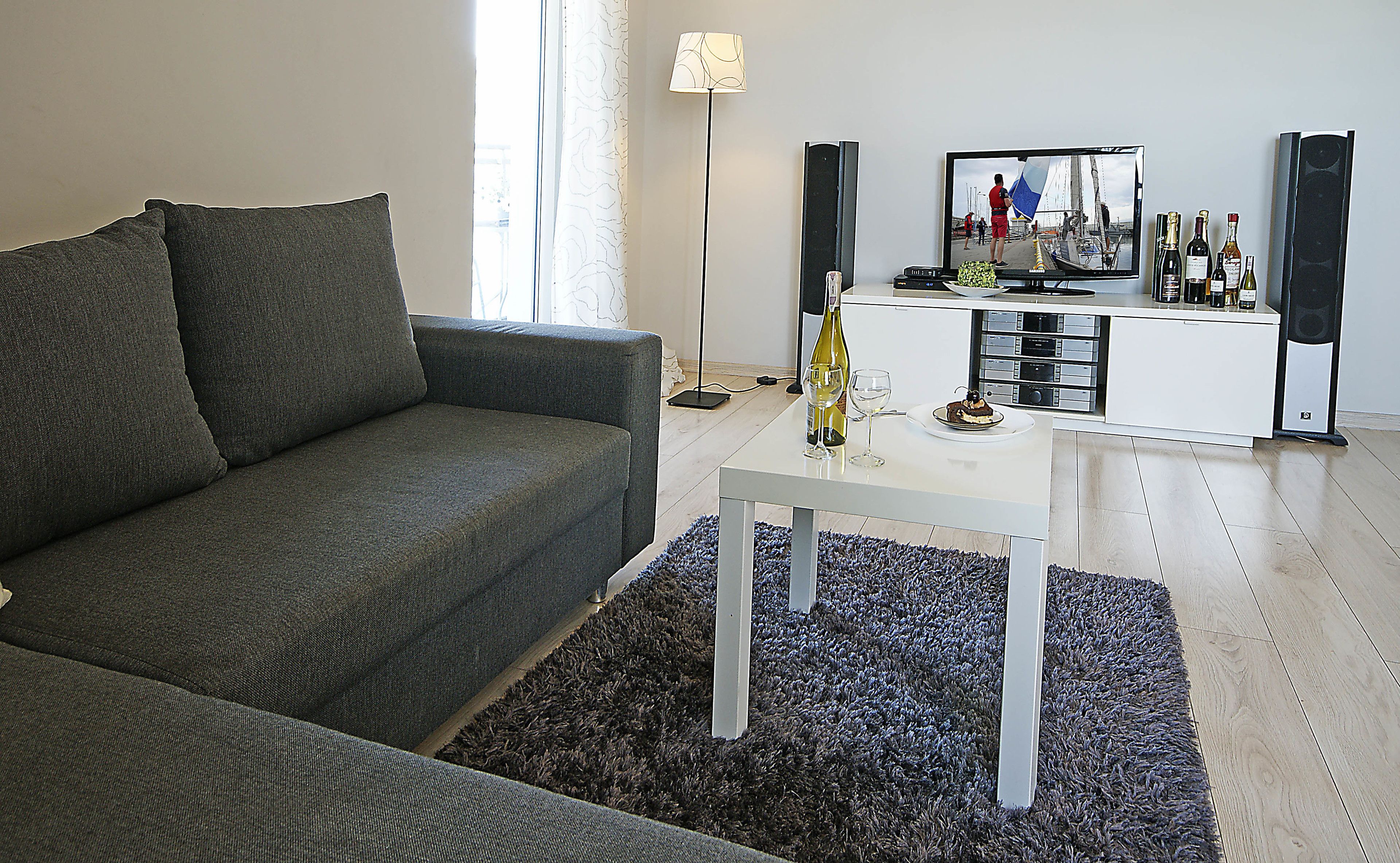 En moderne stue med en grå sofa, et hvidt sofabord og et fjernsyn på et hvidt skab.