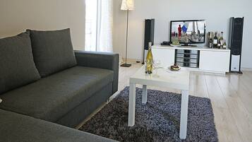 En moderne stue med en grå sofa, et hvidt sofabord og et fjernsyn på et hvidt skab.
