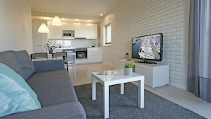 A modern living room with a grey sofa, a white coffee table, and a flat-screen TV mounted on a white brick wall. - IRS ROYAL APARTMENTS - IRS Albatros (Gdansk)