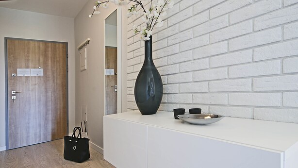 A reception area with a white reception desk, a black vase with flowers, a black handbag, and a metal bowl. - IRS ROYAL APARTMENTS - IRS Albatros (Gdansk)