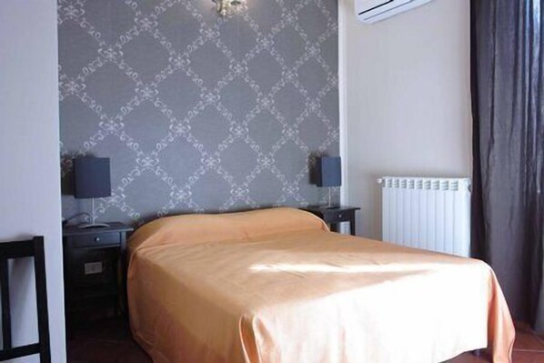 A hotel room with a bed, two nightstands, a wall-mounted air conditioner, and a radiator. - B&B Santa Bibiana (Rome)