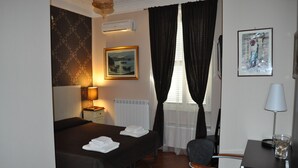 A hotel room with two beds, a desk, a chair, a lamp, and artwork on the walls. - B&B Santa Bibiana (Rome)