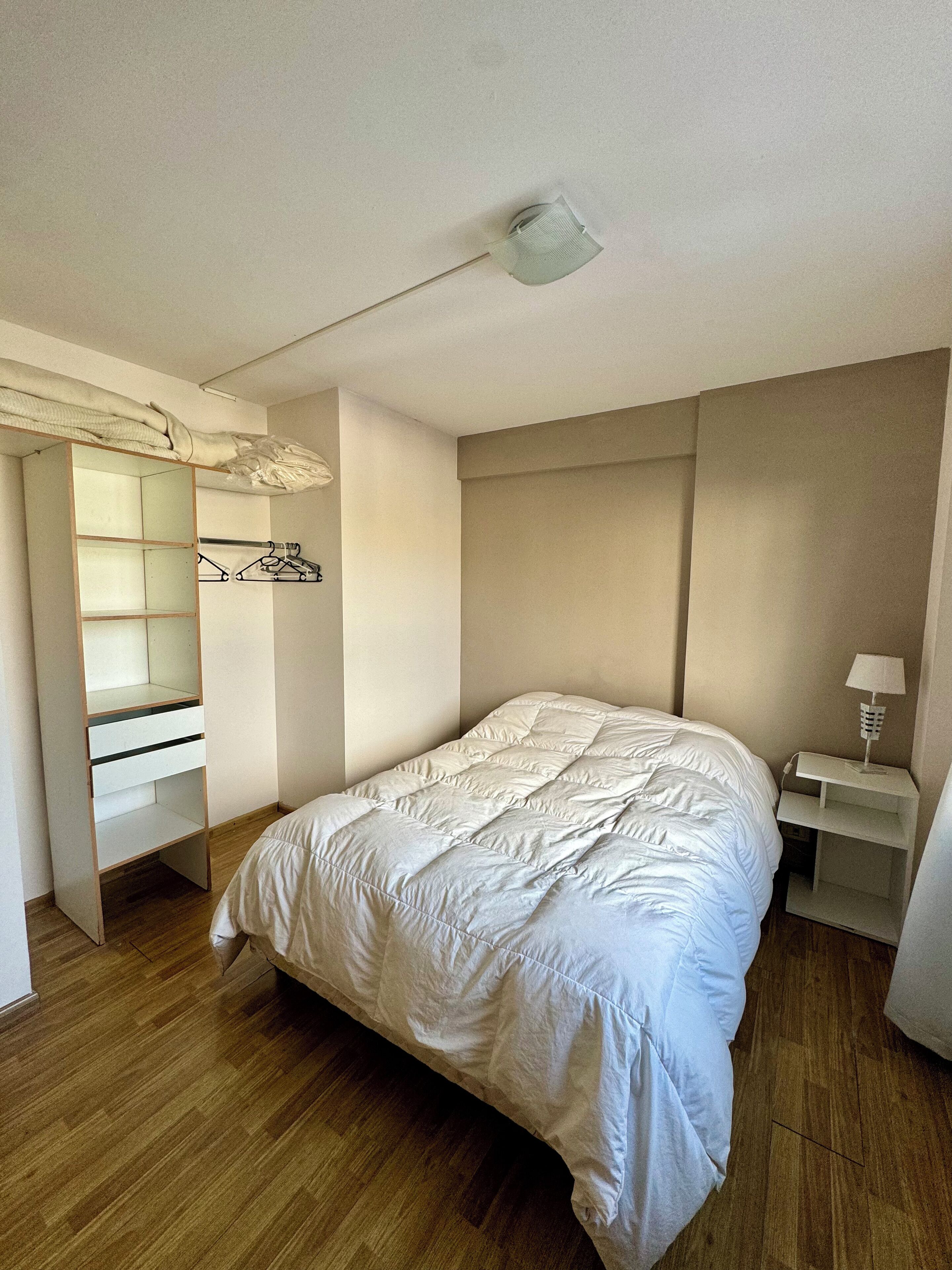 A bedroom with a bed, a wardrobe, a bedside table, and a ceiling light.