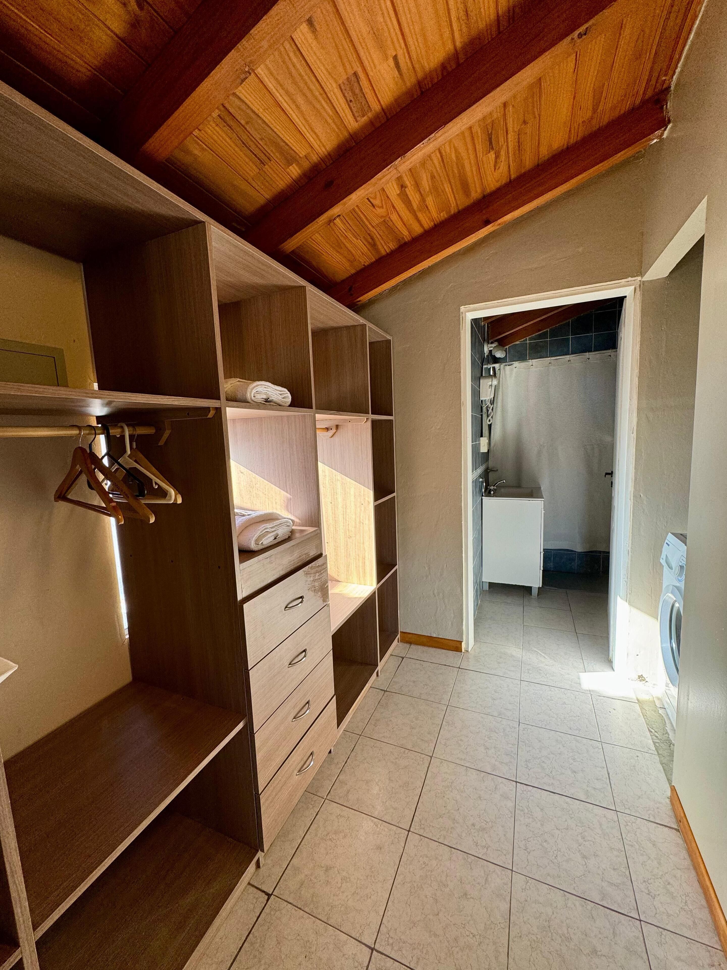 A walk-in closet with wooden shelving, a hanging rack, and a built-in washing machine.