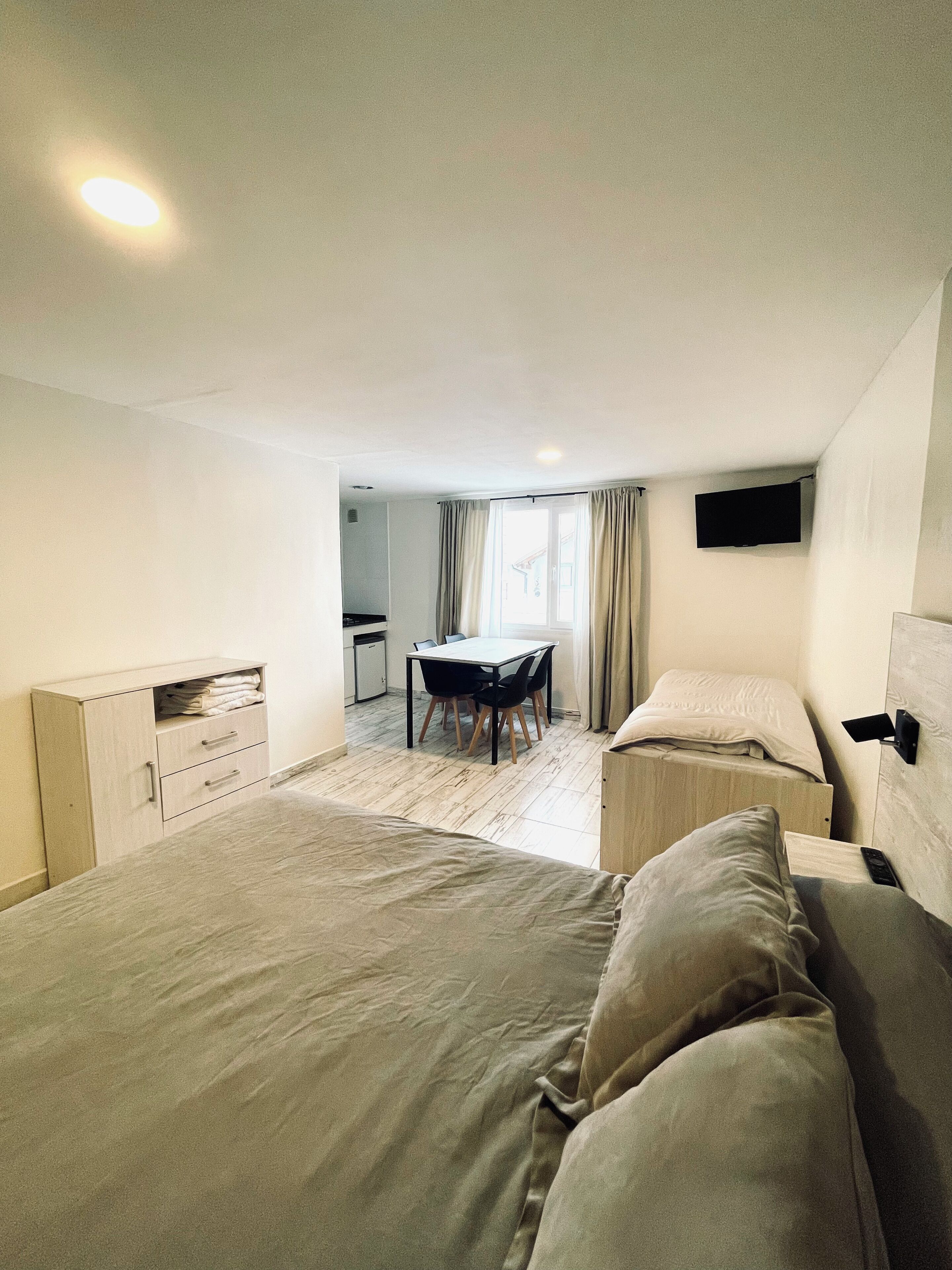 Ein Hotelzimmer mit einem großen Bett, einem Schreibtisch mit Stuhl, einem an der Wand befestigten Fernseher und einem Fenster mit Vorhängen.
