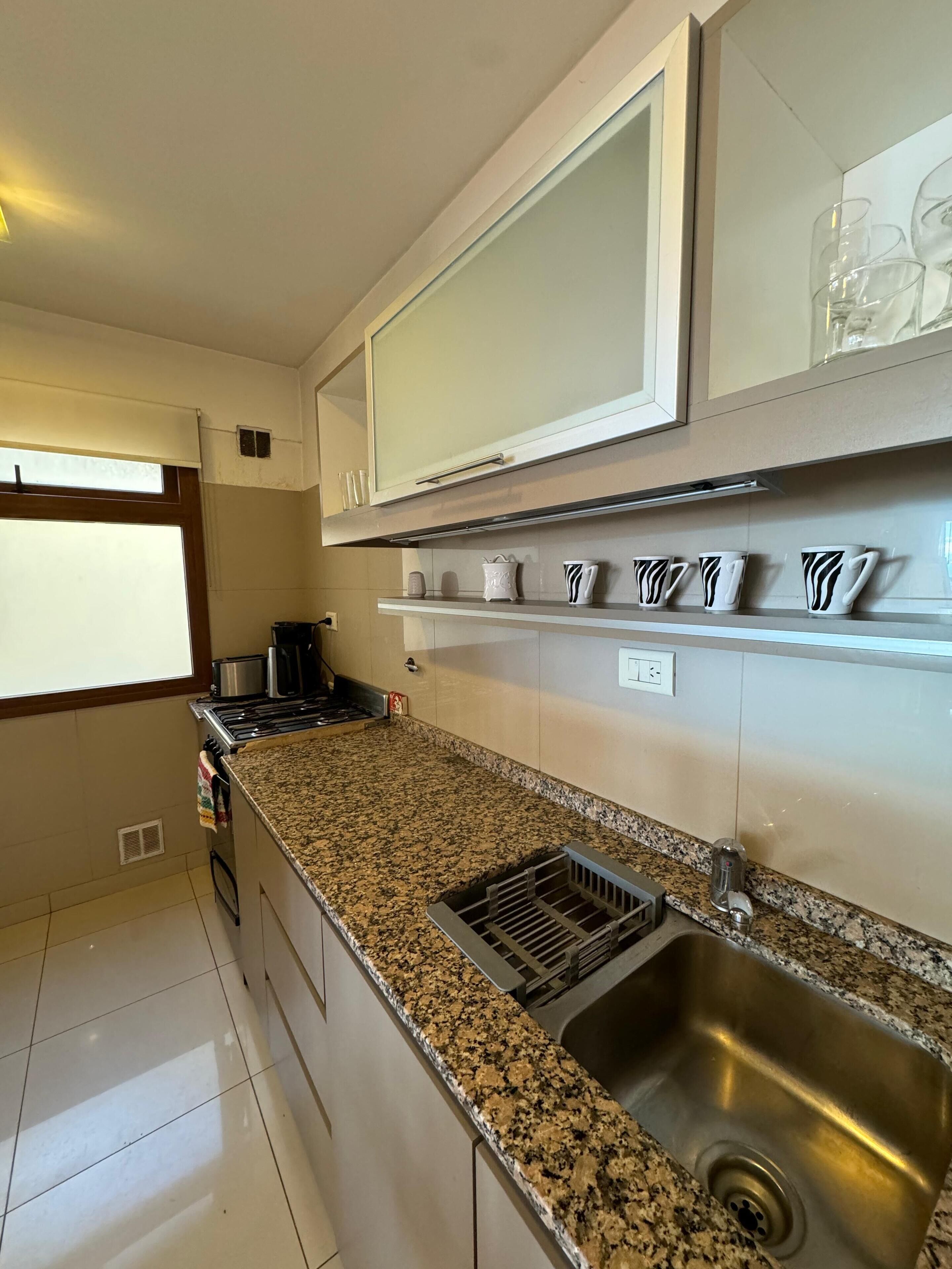 A kitchen with granite countertops, a stainless steel sink, and white cabinets.