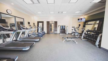 Un gimnasio con cintas de correr, elípticas y un estante con mancuernas.