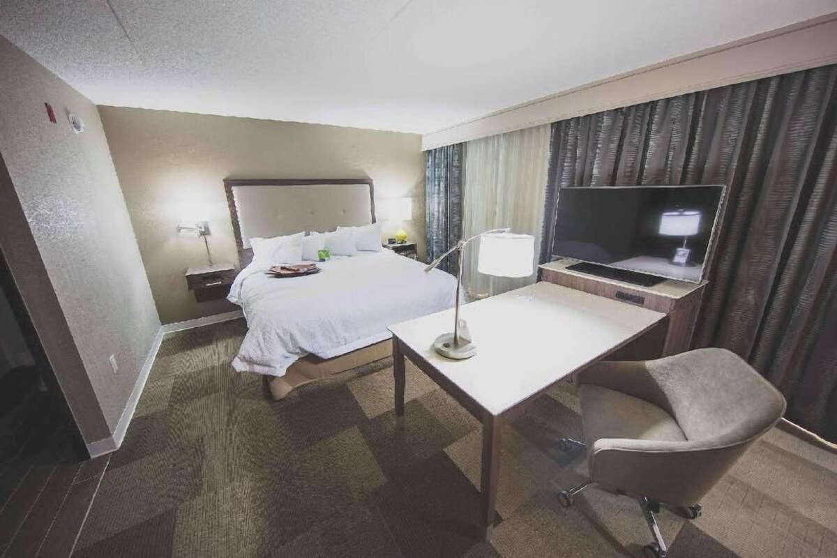 A hotel room with a bed, desk, chair, TV, and curtains.