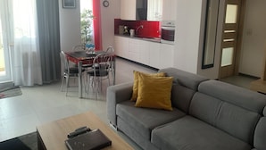 A modern living room with a grey sofa, a wooden coffee table, and a dining area with a red table and chairs. - IRS ROYAL APARTMENTS - IRS Aviator (Gdansk)