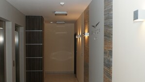 A modern hallway with a wooden panel wall, a light fixture, and a door on the left. - IRS ROYAL APARTMENTS - IRS Aviator (Gdansk)