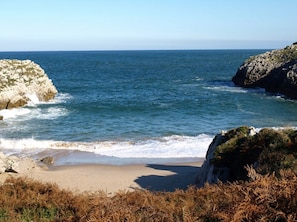 Un paisaje costero con una playa arenosa, afloramientos rocosos y el mar.