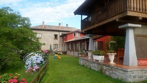 A traditional stone house with a wooden balcony, surrounded by a well-maintained garden with various flowers and a small play area. - Hotel Rural Ovio (Llanes)