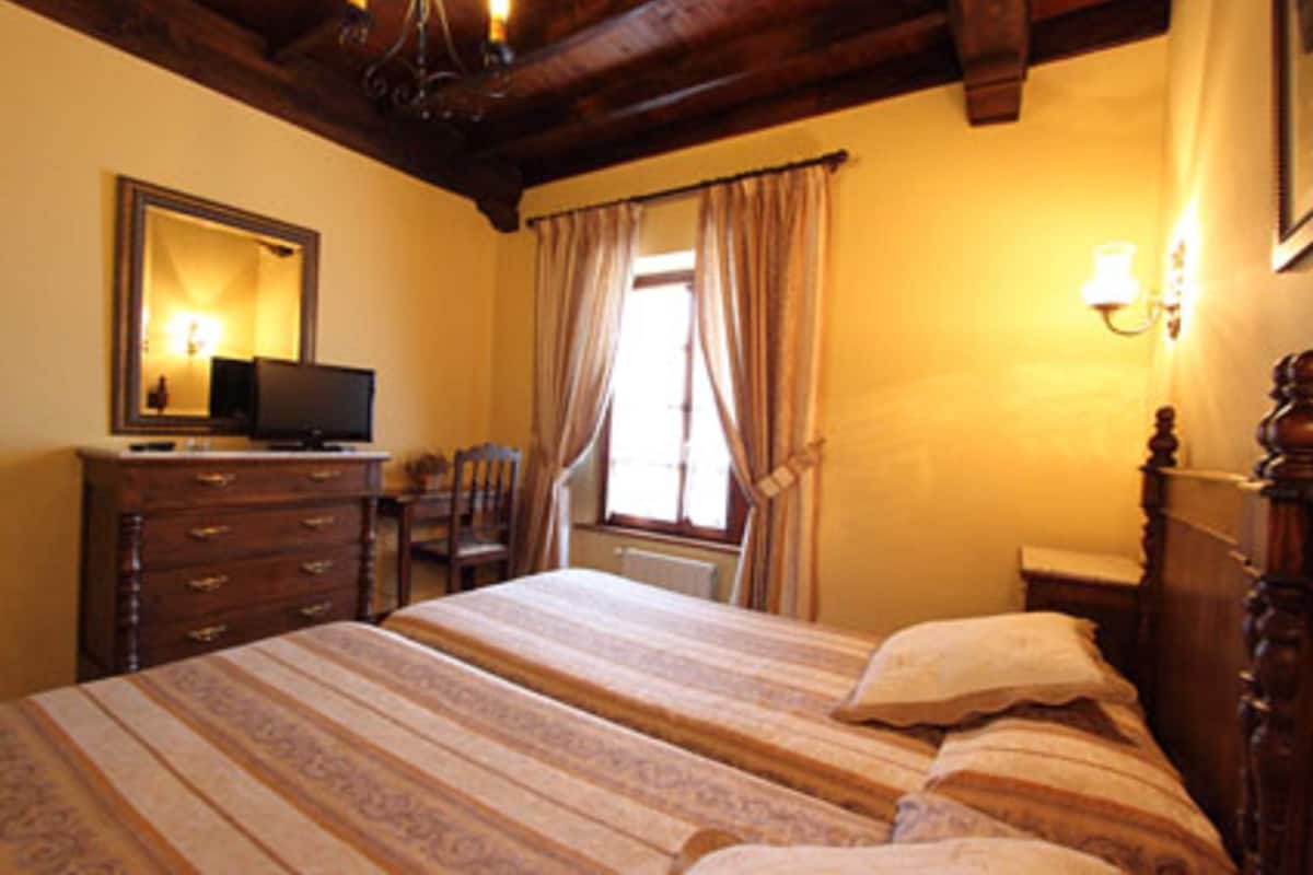 A hotel room with a bed, a dresser, a chair, a desk with a computer, a window with curtains, and a mirror.