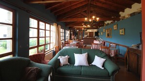 A cozy room with a green sofa, wooden beams, and a dining area with chairs and tables. - Hotel Rural Ovio (Llanes)