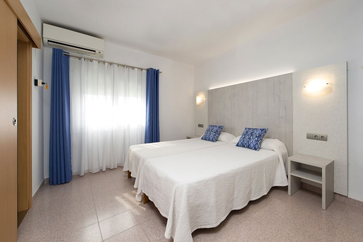 A double bed with a headboard, two pillows, a bedside table, and a wall-mounted light fixture.