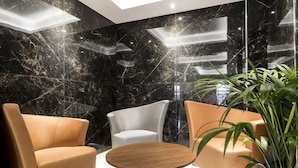 A modern lobby with a marble wall, a round wooden table, and three contemporary chairs. - Hostal Roca (Sant Antoni de Portmany)