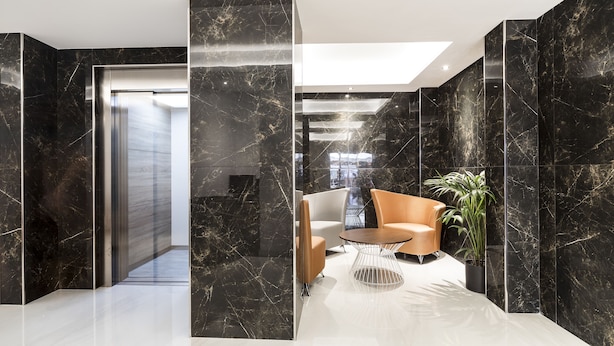 A modern lobby with marble walls, a seating area with a round table, and a potted plant. - Hostal Roca (Sant Antoni de Portmany)