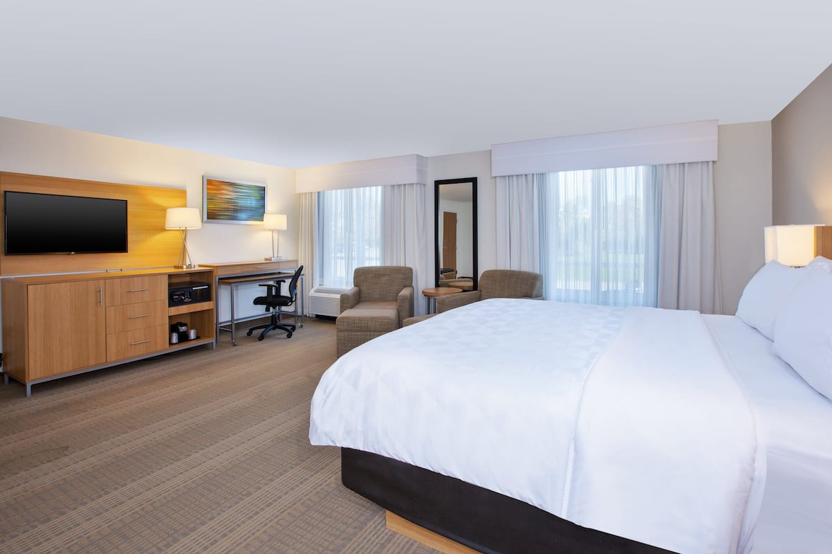 A hotel room with a large bed, a desk with a chair, a television, and a window with curtains.