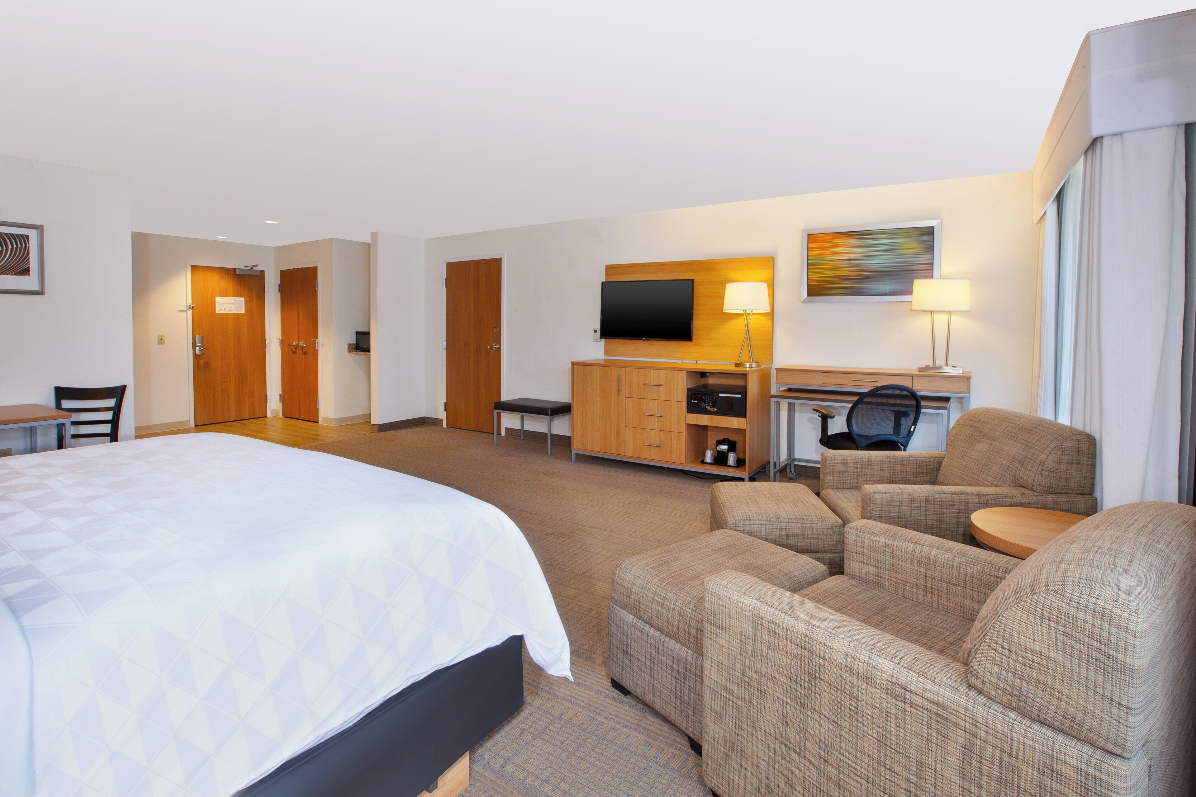 A hotel room with a bed, a desk, a television, and two armchairs.