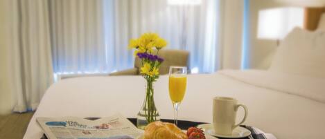 Una bandeja de desayuno ordenada sobre la cama, con un periódico, un croissant, fresas, un vaso de zumo de naranja y una taza.