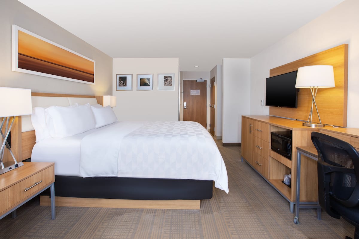 A hotel room with a bed, bedside tables, a desk with a chair, a television, and a microwave.