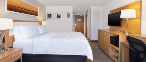 Habitación de hotel con cama, mesitas de noche, escritorio con silla, televisor y microondas.