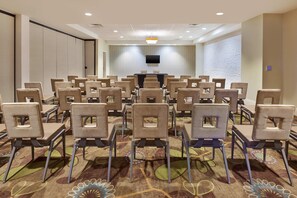 A conference room with rows of beige chairs, a black table, and a flat-screen TV on the wall.